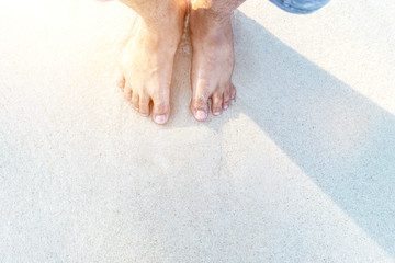 Summer vacation concept. Close up foot of tourist standing on tropical beach and ocean sea with sunset background. Traveler and relax holiday.