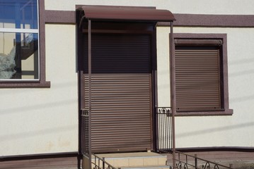 gray wall of the house with a window and door covered with brown roller blinds