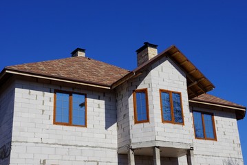 part of the house of gray brick with windows under a brown tiled roof against the blue sky
