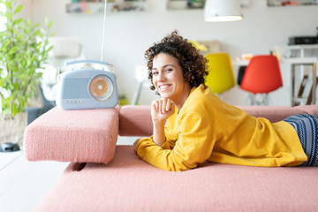 Portrait of happy woman lying on couch listening to music with portable radio at home