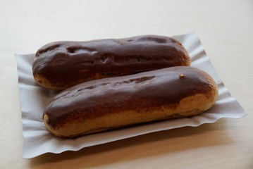 two brown chocolate choux pastries on a gray paper plate