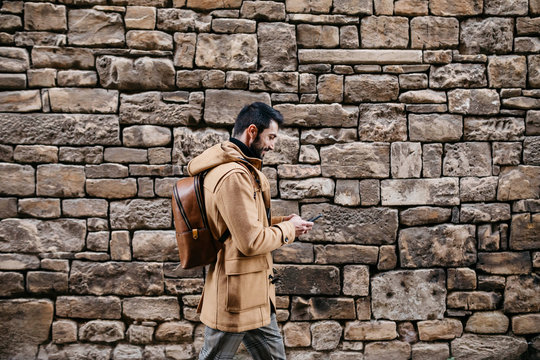 Spain, Igualada, man walking along stone wall using cell phone
