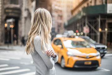 Blonde woman standing on city street and waiting for taxi car at sunny day