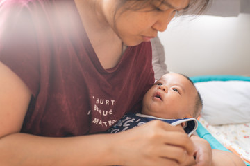 Fototapeta premium Asian women holding smiling infant boy in bedroom