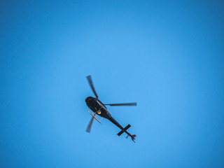 Fototapeta na wymiar A helicopter or chopper hovers overhead on a bright blue sky background.