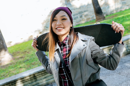 Portrait Of Smiling Young Woman With Skateboard On Her Shoulders