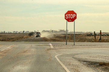 Country Roads - Stop sign with large bullet hole stands by crossroads with pickup truck with...