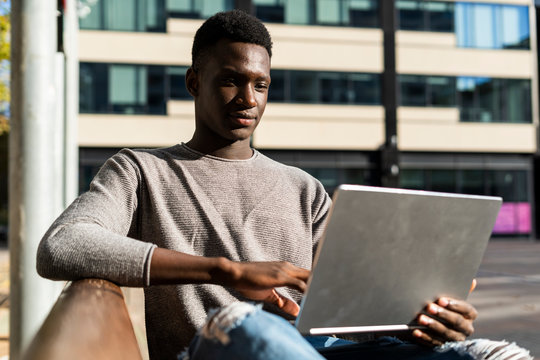 Young man sitting on a bench in the city, using laptop