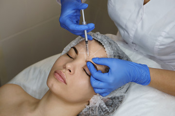 Aesthetic cosmetology. Facelift in spa salon. Beautician makes injections girl in eyebrows....