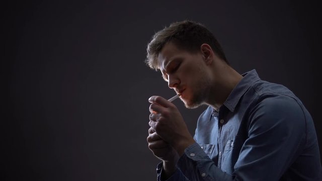 Depressed man smoking isolated on dark background, thinking about life problems