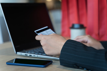 Business women. Young Asian girl sits on the chair enjoys online shopping. Young female purchases thing online using mobile phone, laptop, credit card