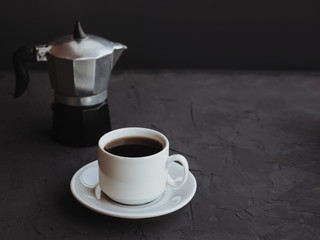White cup of coffee and coffee maker on dark background