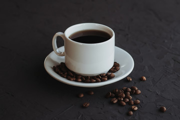 White cup of coffee and coffee beans on a dark background