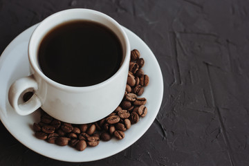 White cup of coffee and coffee beans on a dark background