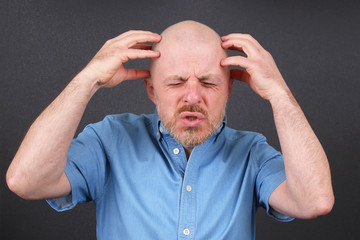 bearded man is very emotionally stressed holding his hands near his head
