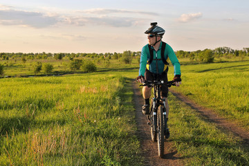 Obraz premium cyclist rides on the road in a field on a bright sunny day.