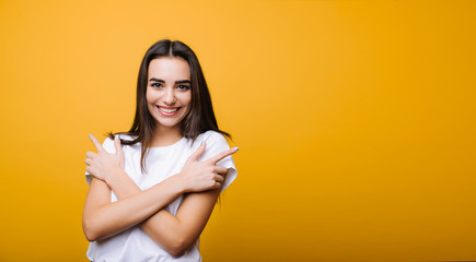 Obraz premium Beautiful young attractive girl with long dark hair looking at camera laughing while embracing herself isolated over yellow background.
