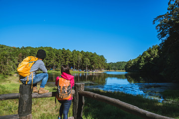 A Couple travelers with backpack standing on top Of the viewpoint nature a beautiful, Enjoy the sunrise on the foggy lake surface.