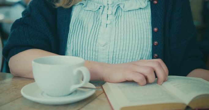 Young woman drinking coffee and reading book in cafe
