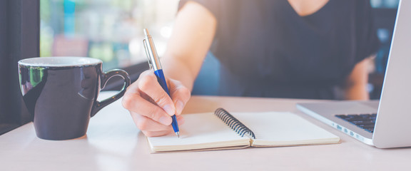 Business woman's hand is writing on a notebook with a pen.