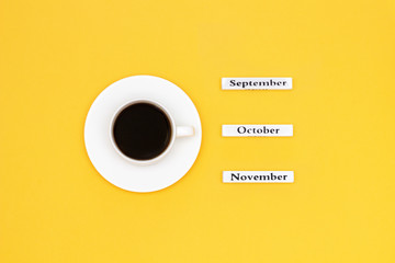 Wooden calendar autumn months September October November and Cup of black coffee aimed at October on yellow background. Concept Top view Flat Lay Copy space