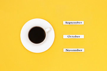 Wooden calendar autumn months September October November and Cup of black coffee aimed at September on yellow background. Concept Top view Flat Lay Copy space
