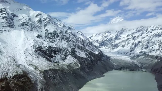 Panoramic aerial shot of valley with glacial lake and stream and picturesque mountain ranges covered with snow