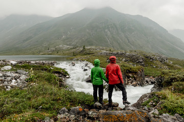 Couple of tourists standing by the mountain river on a foggy summer day in the rain