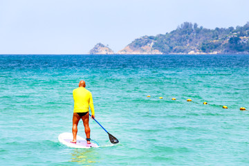 Man On Stand Up Paddle Board in sea. Water fun on beach.