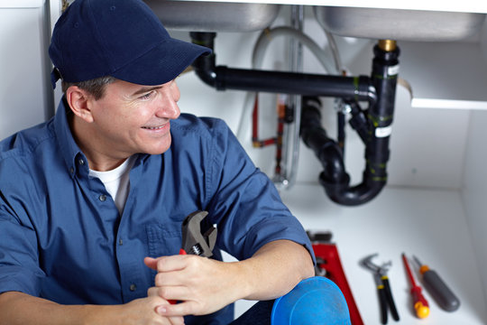 Smiling plumber repairs a sink.
