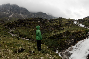 Woman of tourists standing by the mountain river on a foggy summer day in the rain