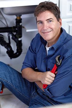 Smiling plumber repairs a sink.