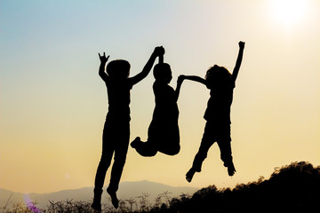 Silhouette of happy children jumping playing on mountain meadow at sunset time