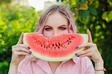 Beautiful young woman with pink hair holding juicy watermelon close to the face