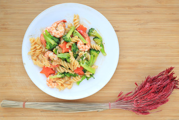 Fried Spiral Macaroni with shrimp and vegetables decorated with dried flower on wood background.