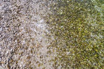 Stones under water. Sea pebbles on the beach. Sea pebbles on the beach sand with transparent water. Natural sea stones closeup. Beach smooth pebbles. Tourism and travel themed. Vacation background.
