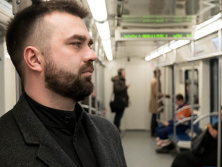 Handsome bearded man dressed in wool coat stands in metro carriage tired after hard work day