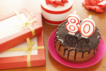 Birthday celebration at eighty years. A cake with burning candles in the form of numbers and a lot of gifts on a table