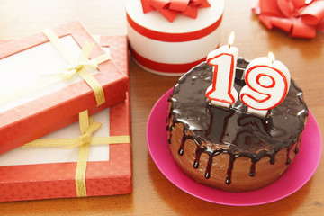 Birthday celebration at nineteen years. A cake with burning candles in the form of numbers and a lot of gifts on a table