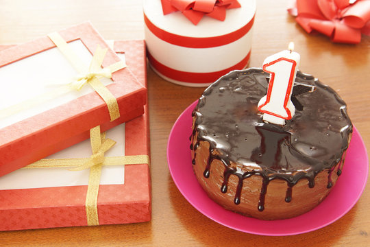 Birthday celebration at one year. A cake with burning candle in the form of number and a lot of gifts on a table