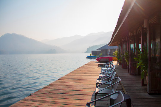 Soft sunlight in the morning and the terrace of floating home stay on the lake with chairs and table for tourists to relaxing time or time of freedom. The mountain view in background.