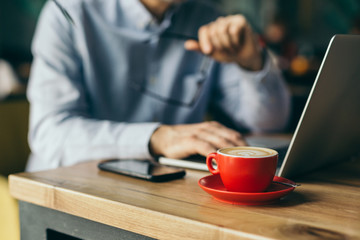 coffee break concept. cup of coffee in foreground and blurred man using laptop in background