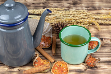 A Tin cup of bael tea and terpot on wooden table.