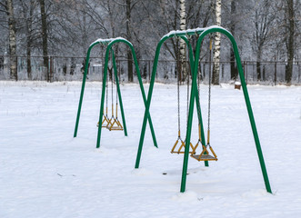 playground with swings, benches, slide and sports units in  snow.