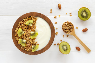 Top view of yogurt in a wooden bowl with granola,fresh kiwi, mint, almond and spoon on blue wooden table. Health food concept.