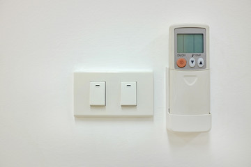 Electric switch and air conditioner remote control on the white wall.
