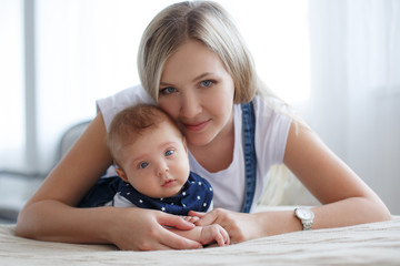 Young mother holding her newborn child.Woman and new born boy relax in a white bedroom.A young...
