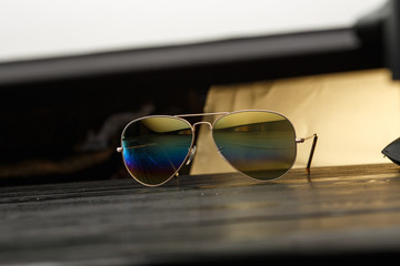 aviators sunglasses with mirrored color lenses made of glass in a gold metal frame covered with gold matte dusting on a black wooden background