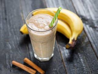 Banana smoothie with cinnamon in glass on wooden background