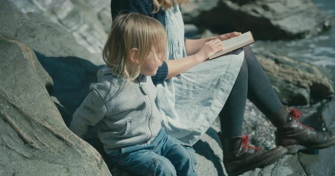 Young mother reading book with toddler by the sea
